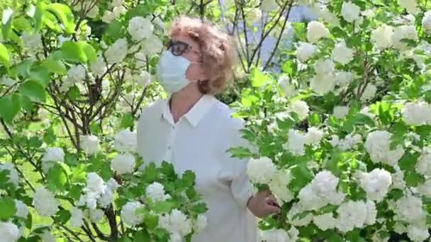 Seorang wanita tua dalam topeng pelindung mengendus pohon apel mekar — Stok Video