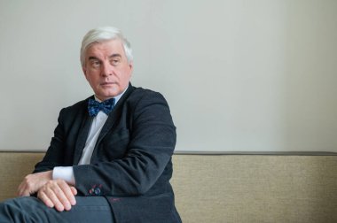 Takım elbiseli, papyonlu ve koltukta oturan kendine güvenen gri saçlı bir iş adamı. Üst düzey erkek patron ofiste..