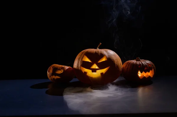 Cartão de Halloween. jack o lanterna com velas brilham sobre um fundo preto. Uma fileira de abóboras assustadoras com caretas esculpidas fuma no escuro. — Fotografia de Stock