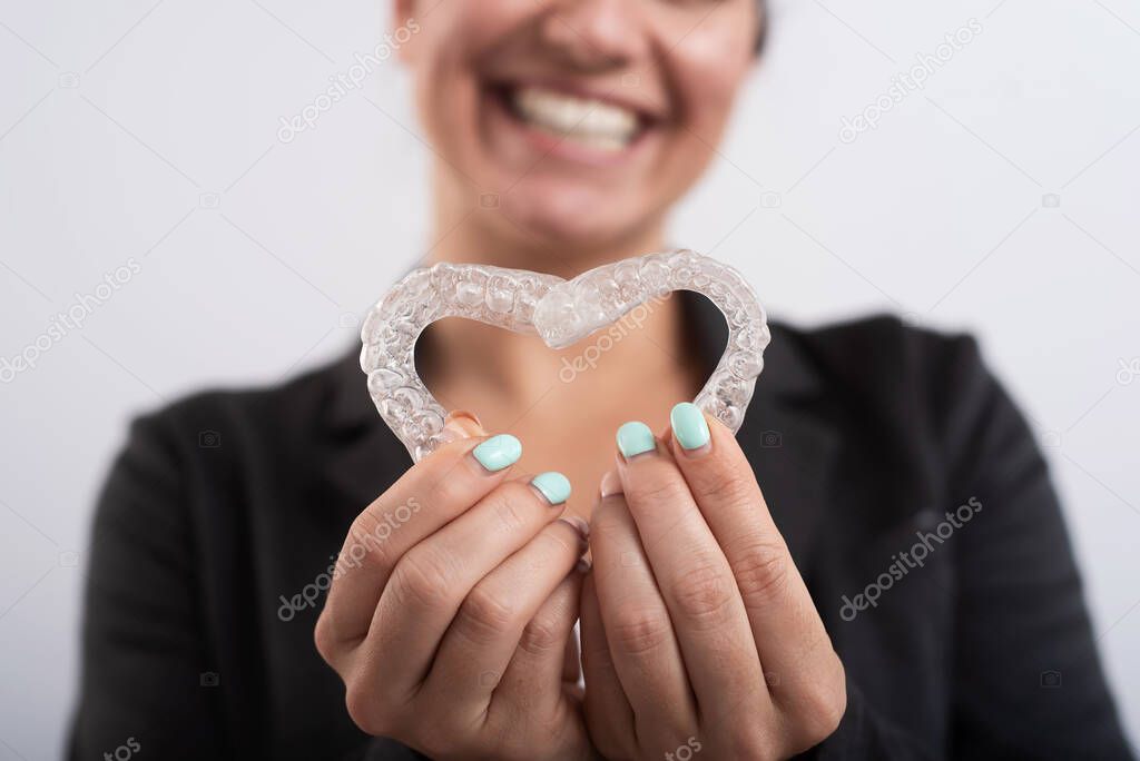 Caucasian woman holding two transparent heart-shaped aligners