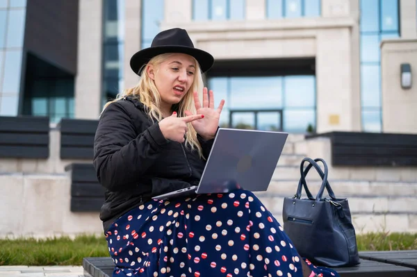 Ung kvinna talar teckenspråk på ett videosamtal på en bärbar dator utomhus. Den dövstumma flickan kommunicerar med gester — Stockfoto