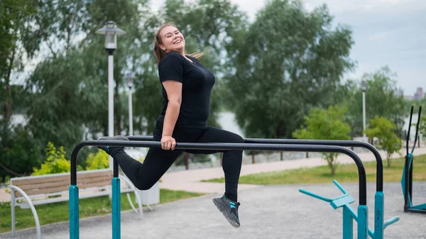 Plumpe junge Frau, die draußen auf dem unebenen Stufenbarren Übungen macht. Kaukasisches Mädchen macht Liegestütze — Stockfoto