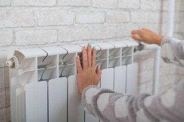 Isıtma radyatörünün ısısını düzenleyen kadın elinin yakın çekimi.