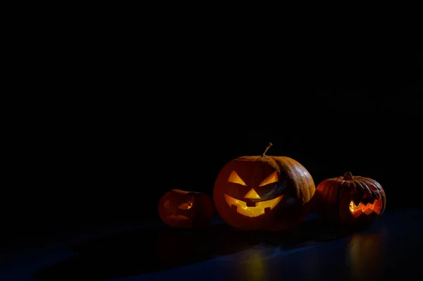 Halloweenská karta. Jack o lucerna se svíčkami zářit na černém pozadí. Řada strašidelných dýní s vyřezávanými grimasami kouří ve tmě. — Stock fotografie