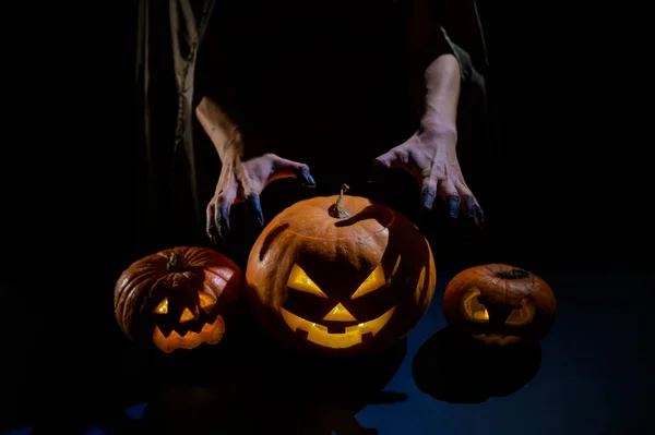 Zbliżenie żeńskich dłoni na dyni na Halloween w ciemnym studio. Czarownica trzyma latarnię. — Zdjęcie stockowe