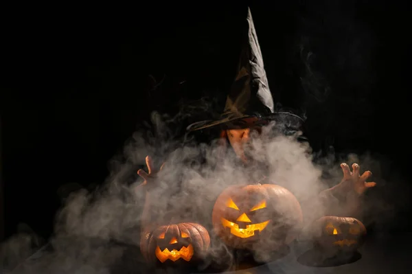 Zlá čarodějnice seslala kouzlo na dýně. Portrét ženy v karnevalovém halloweenském kostýmu ve tmě — Stock fotografie