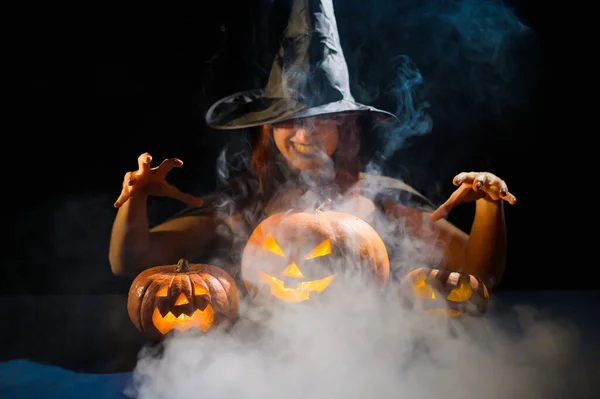 Kötü cadı balkabaklarına büyü yapıyor. Karanlıkta cadılar bayramı kostümü giymiş bir kadının portresi. — Stok fotoğraf