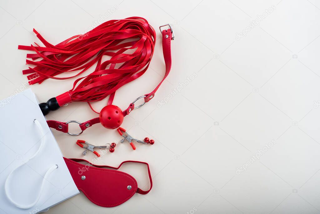 Top view of a red bdsm set in a white paper bag on a white background. Flat lay from sex toys