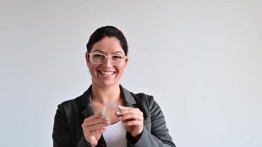 Kadın gülümsüyor ve ısırık düzeltmesi için şeffaf plastik bir hizalayıcı tutuyor.