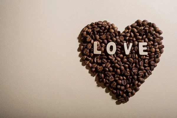 Chicchi di caffè nella forma di un cuore e l'amore di iscrizione su uno sfondo — Foto Stock