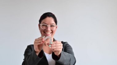 Kadın gülümsüyor ve ısırık düzeltmesi için şeffaf plastik bir hizalayıcı tutuyor.