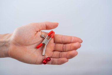 Beyaz arka planda bir kadın elinin meme ucu kıskaçlarını kapat. BDSM seks oyuncağı