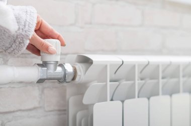 Isıtma radyatörünün ısısını düzenleyen kadın elinin yakın çekimi.