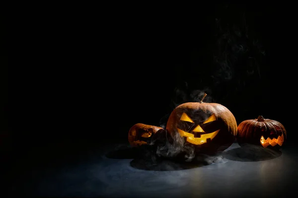 Cartão de Halloween. jack o lanterna com velas brilham sobre um fundo preto. Uma fileira de abóboras assustadoras com caretas esculpidas fuma no escuro. — Fotografia de Stock