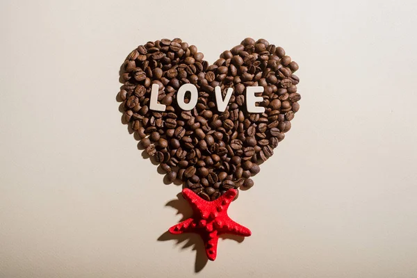 Vista superior de grãos de café na forma de coração lettering amor e estrela-do-mar vermelho — Fotografia de Stock