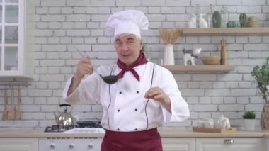 Erkek aşçı çorbanın kokusundan zevk alır ve mutfaktaki kepçeyle tadına bakar.