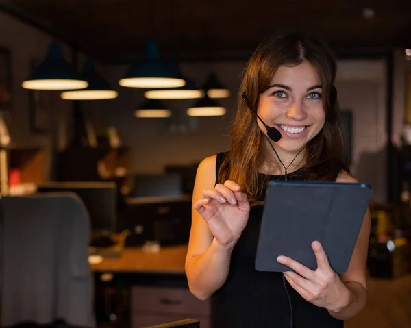 Hermosa mujer de negocios usando en un auricular está sosteniendo una tableta digital en la oficina —  Fotos de Stock