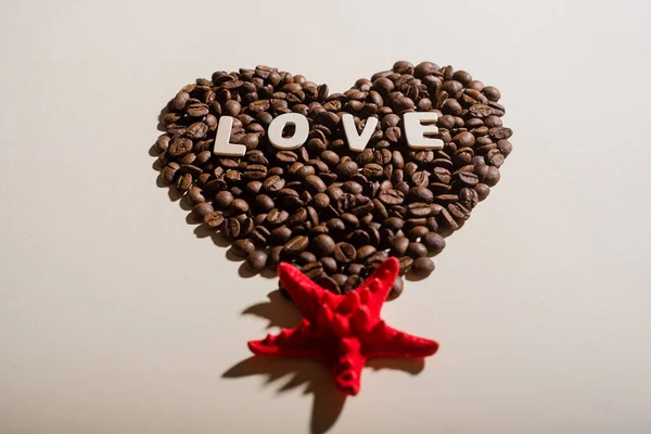 Vista superior de granos de café en forma de corazón con letras de amor y estrellas de mar rojas — Foto de Stock