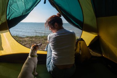 Bir kadın ve bir köpek deniz kenarındaki bir turist çadırında oturuyorlar. Doğada eğlence..