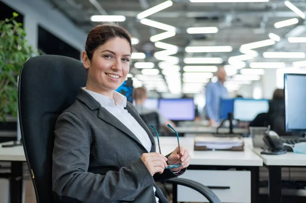 Успешная деловая женщина сидит за своим столом в офисе с очками в руках — стоковое фото