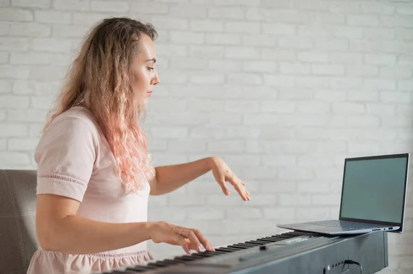 Música conceito de aprendizagem online. Uma mulher conduz aulas de distância sobre tocar piano via comunicação por vídeo em um laptop — Fotografia de Stock