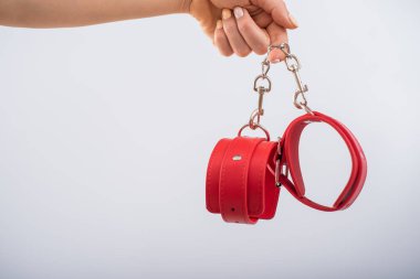 Beyaz arka planda kırmızı deri kelepçeler ve kadın elleri. BDSM aksesuarları