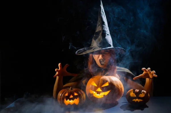 Zlá čarodějnice seslala kouzlo na dýně. Portrét ženy v karnevalovém halloweenském kostýmu ve tmě — Stock fotografie