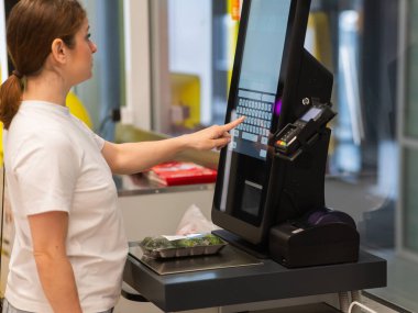 Bir kadın self-servis kasasında salatalık tartır.