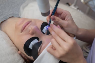 Kirpik uzatma prosedüründen geçen bir kadın ultraviyole lamba kullanıyor.