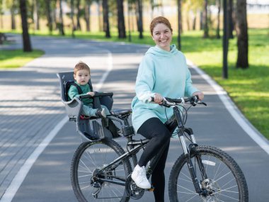 Küçük oğluyla bisiklete binen beyaz bir kadın arkasında çocuk koltuğunda oturuyor.