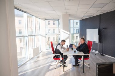 Masada otururken akıllı telefon kullanan iki beyaz adam.