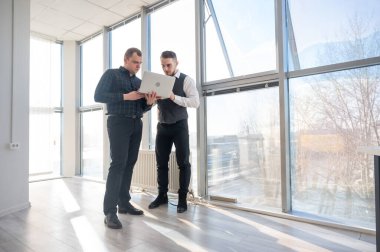 İki beyaz adam dizüstü bilgisayara bakıyor ve iş tartışıyorlar.