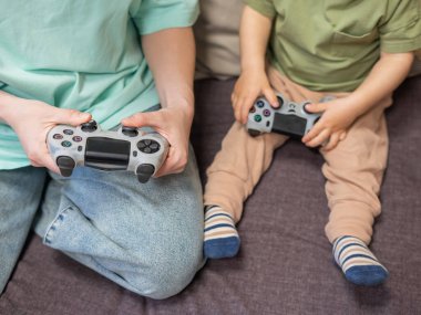 Beyaz kadın küçük oğluna konsol oynamayı öğretiyor. Oyun kolu ellerinde.