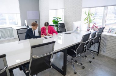 Kadın ve erkek ofiste otururken konuşuyorlar.