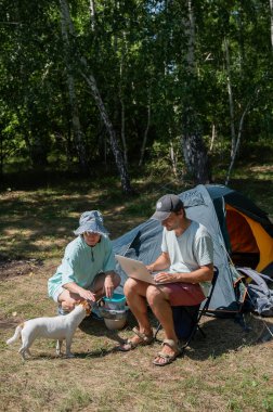 Kamp yaparken dizüstü bilgisayarda çalışan beyaz bir adam. Çift doğada dinleniyor.