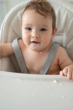 Ekşi kremaya bulanmış sevimli erkek bebek yüksek bir sandalyede oturuyor.