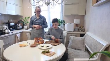 Kafkasyalı çocuk annesiyle evde hamburger pişiriyor.