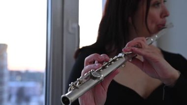 Beyaz kadın pencere eşiğinde flüt çalıyor.