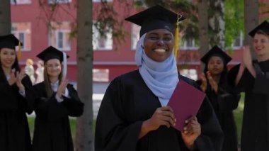 Sınıf arkadaşları onu alkışlarken genç Afrikalı kadın diplomasını tutuyor.