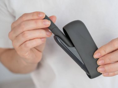 Bir kadın, tütün ısıtma sistemini şarj aletinden çıkarır. Elektronik sigara.