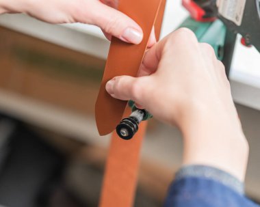 Deri işçisi atölyede kemer için deri şeritlerini öğütüyor.