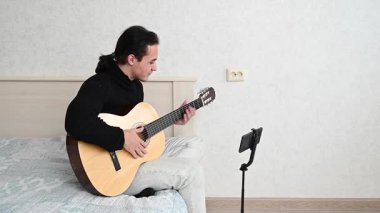 Genç adam kendini akıllı telefondan çekerken akustik gitar çalıyor. Parmak Biçimi