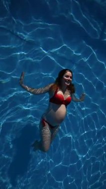 Havuzda kırmızı bikinili hamile bir kadın. Ağır çekim. Dikey video