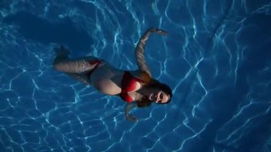 Havuzda kırmızı bikinili hamile bir kadın. Ağır çekim. Dikey video