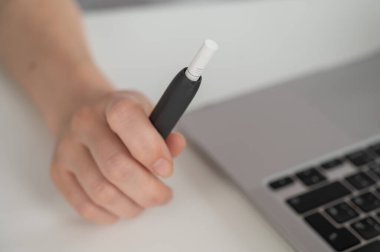 Bir kadın dizüstü bilgisayarla uğraşırken elektronik sigara içiyor. Tütün ısıtma sistemi