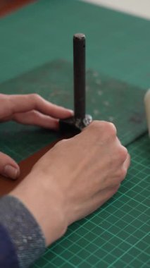 Deri işçisi bir atölyedeki kemerden bir parça deri kesiyor.