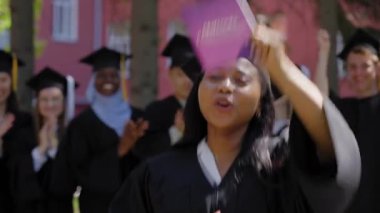 Sınıf arkadaşları onu alkışlarken genç Afrikalı kadın diplomasını tutuyor.