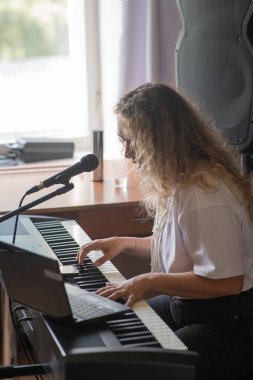 Beyaz kadın mikrofona şarkı söylüyor ve sentezleyici çalıyor. Bilgisayarda çevrimiçi ders