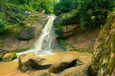 KAMENNOMOSTSKY, ADYGEA / RUSSIA - 29 Temmuz 2020: Bir grup turist Mishoko nehri üzerindeki güzel şelalenin kaynağına doğru dağ yamacına tırmanıyor