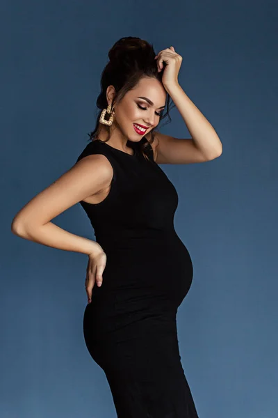 Pregnant european woman in black dress in dark flat, stylish and happy pregnant woman in apartments, beautiful pregnant woman in dark studio